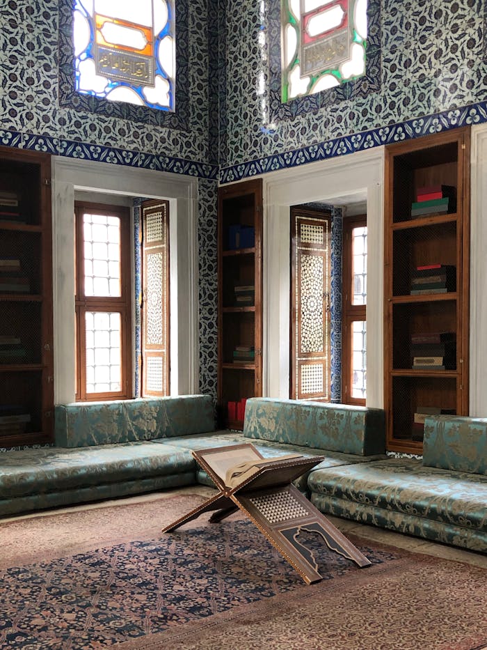 Peaceful corner in a mosque with open Quran and intricate stained glass windows.